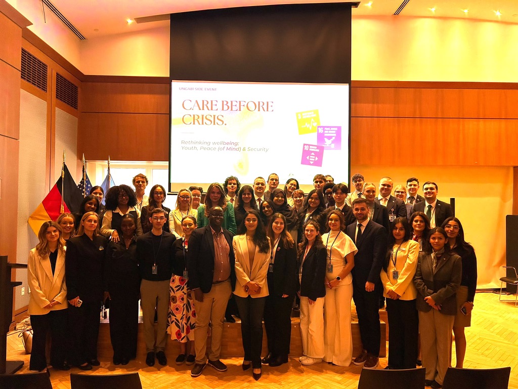 Group photo of participants at the Care Before Crisis side event, with the event title on screen